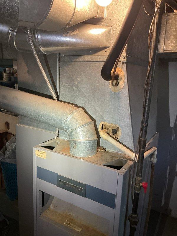 Responded to service call for water leaking from 38-year-old furnace located in basement. Upon inspection, observed visible water staining and discoloration on concrete floor surrounding base of unit, confirming active leak condition. Documented existing HVAC installation including furnace cabinet, metallic ductwork system with flexible and rigid connections, gas line with shutoff valve, and associated mechanical components. Given the advanced age of the equipment and absence of warranty coverage, provided assessment and recommendations for addressing the water leak issue.