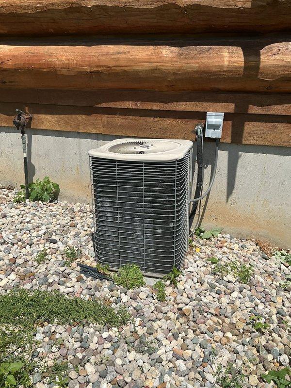 Responded to no cooling complaint on 22-year-old residential air conditioning system. Upon arrival, performed visual inspection of outdoor condenser unit and found significant debris accumulation inside cabinet affecting component operation. Opened unit and documented interior condition showing dirt and organic material buildup around base and electrical components. Assessed cylindrical motor/compressor assembly, electrical connections, and refrigerant line routing. Unit showed signs of age-related wear consistent with equipment exceeding typical service life. Photographed exterior installation against foundation wall with river rock landscaping and documented internal cabinet condition including wiring, capacitor connections, and debris accumulation. Completed diagnostic assessment and provided findings to customer regarding system condition and cooling failure. Given the advanced age of the equipment at over two decades old, discussed replacement options as most cost-effective long-t