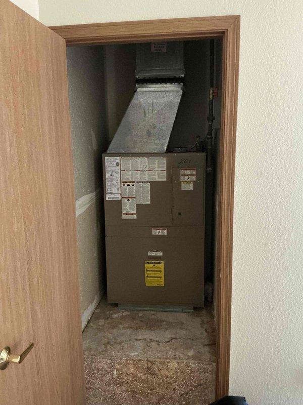 Provided estimate for replacement of Magic Pack HVAC system serving unit 201. Current equipment, installed in 2003, has a hole in the A/C component and requires full replacement. The natural gas furnace and air conditioning unit are located in an interior closet within the unit, with ductwork transitioning through the ceiling plenum and electrical panel accessible nearby.