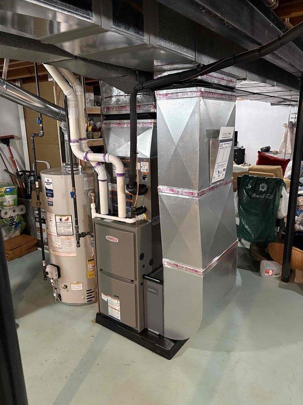 Completed full HVAC system installation including a 70,000 BTU furnace, 2-ton air conditioning unit, and water heater in basement mechanical room. Installed furnace with metallic ductwork on platform, positioned water heater with copper piping connections and blue-handled valves, and mounted exterior AC unit with associated electrical disconnects and refrigerant line connections. Reconnected all electrical and plumbing systems, installed PVC condensate drainage lines through exterior wall, and secured all ductwork and support systems per code requirements.