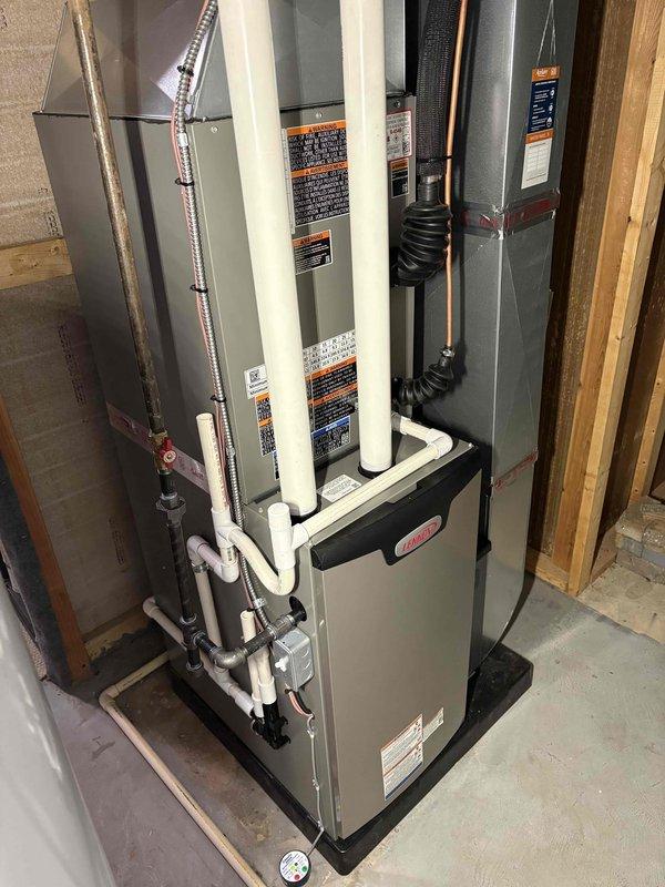 Completed full HVAC system installation including a 70,000 BTU furnace with humidifier and 3-ton air conditioning unit. Indoor equipment installed on platform base in basement with proper condensate drainage via PVC piping, flexible ductwork connections, and refrigerant line sets between units. Outdoor Lennox condenser unit positioned on pad with electrical and refrigerant connections completed to manufacturer specifications.