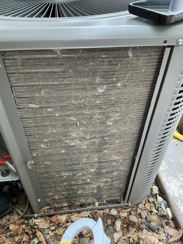 Performed annual preventive maintenance on a 4-year-old air conditioning system. Inspected outdoor condenser unit and found heavily soiled air filter/coil with significant dirt and debris accumulation requiring cleaning. Removed organic debris including leaves, twigs, and mulch from base of unit and around components. Cleaned condenser coils and filter panel to restore proper airflow. Verified electrical readings using clamp meter, measuring amperage at 0.59A and voltage at 0.2V during testing. Checked refrigerant levels, inspected all electrical connections, and confirmed proper system operation. Unit tested and found to be functioning within normal parameters upon completion of maintenance.