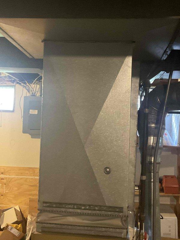 Completed HVAC system replacement estimate for duplex unit, documenting existing furnace and air handler equipment in basement mechanical room. Photographed current system configuration including gray metal furnace unit with horizontal grille vent, cream-colored air handler with metallic exhaust piping, black flexible ductwork routing, and electrical panel connections to assess replacement requirements and system specifications.