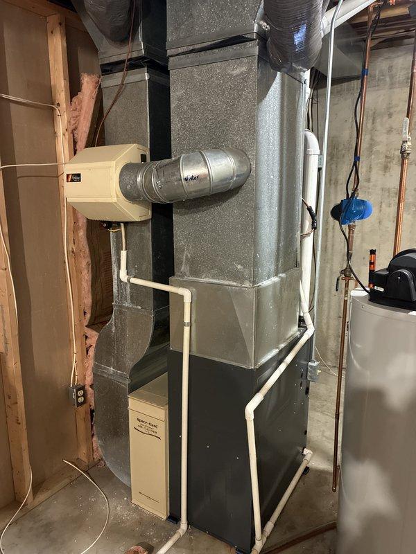 Conducted comprehensive assessment of 15-year-old residential HVAC system for complete replacement estimate due to unrepairable refrigerant leak with obsolete refrigerant type. Inspected basement-mounted gas furnace with integral blower assembly, documented existing ductwork configuration including flexible supply runs and humidifier integration, evaluated electrical connections and gas line condition showing visible oxidation on copper supply piping. Photographed outdoor condensing unit and indoor air handler components to document current system layout and specifications for accurate replacement sizing and equipment selection.