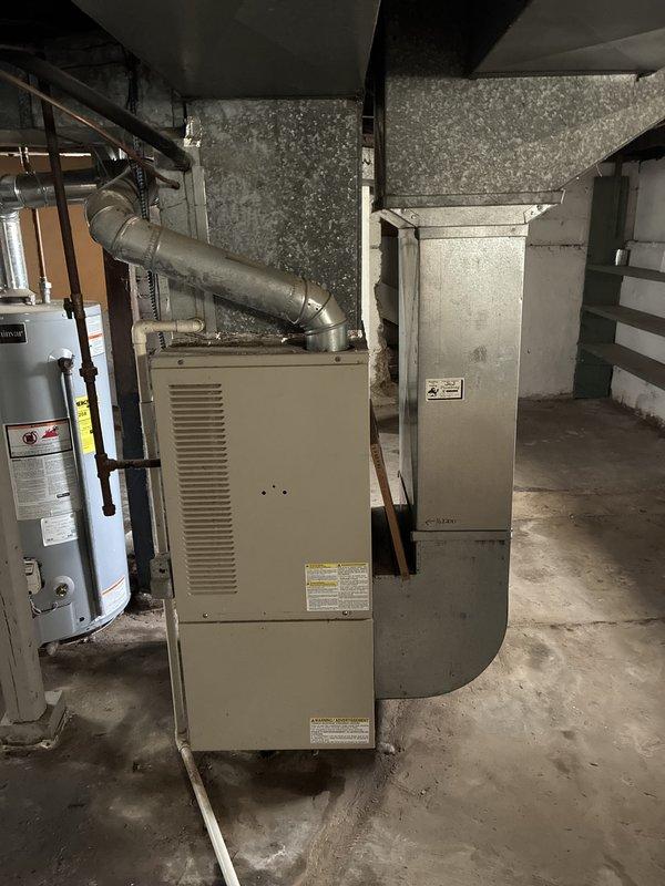 Conducted in-home estimate for replacement of 23-year-old furnace system located in basement utility area. Inspected existing beige/cream-colored furnace unit with associated ductwork, metal plenum, and ventilation components to assess replacement requirements and system configuration. Documented current equipment layout including furnace positioning, duct routing, water heater proximity, and available workspace for future installation planning.