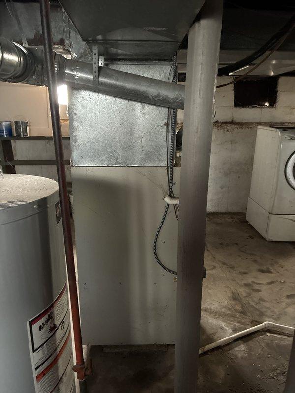 Conducted in-home estimate for replacement of 23-year-old furnace system located in basement utility area. Inspected existing beige/cream-colored furnace unit with associated ductwork, metal plenum, and ventilation components to assess replacement requirements and system configuration. Documented current equipment layout including furnace positioning, duct routing, water heater proximity, and available workspace for future installation planning.