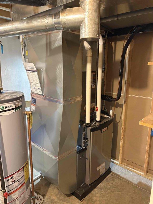 Completed full HVAC system installation including a 90,000 BTU gas furnace and 3-ton Lennox air conditioning unit with outdoor condenser positioned on concrete pad against exterior wall. Installed humidifier on left side of furnace, connected refrigerant lines with proper insulation, mounted electrical disconnect box, and reconnected all ductwork and utilities in basement mechanical room. All permits obtained, system tested and operational.