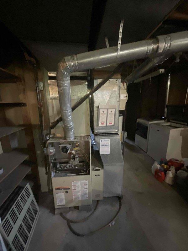 Completed on-site evaluation of 16-year-old HVAC system for replacement estimate. Inspected existing furnace with open access panel revealing burner assembly, internal components, and ductwork configuration in basement utility area. Evaluated exterior AC compressor/condenser unit mounted on turquoise equipment stand against building exterior. Assessed system for both partial component replacement options including compressor/condenser, inducer motor, and blower motor, as well as full system replacement recommendation due to age of equipment reaching end of typical service life.