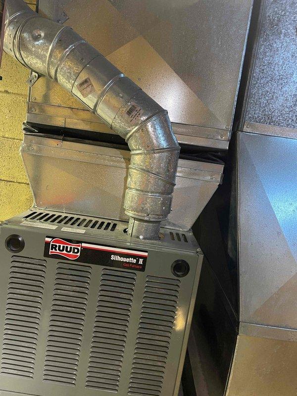 Conducted site assessment for central air conditioning installation in a 1970s home currently equipped with a Ruud Silhouette II gas furnace but no existing AC system. Evaluated basement mechanical room layout, existing ductwork configuration, and available space for condenser and air handler placement. Photographed current HVAC setup including furnace location, flexible ductwork routing, water heater proximity, and utility room constraints to develop comprehensive whole-house cooling solution estimate.