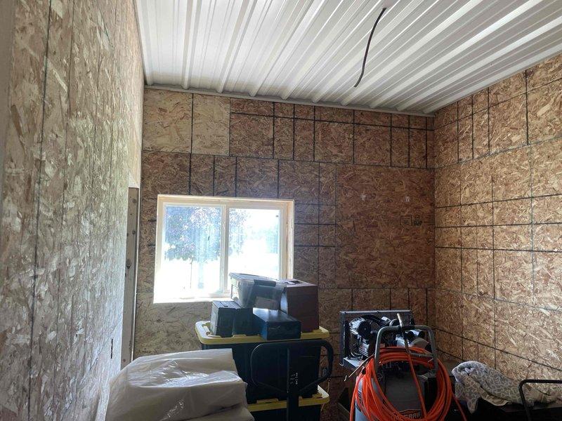 Conducted site evaluation for new mini-split system installation in finished garage/workshop space with OSB wall panels, corrugated metal ceiling, and epoxy-coated flooring. Assessed installation requirements and documented conditions for ductless heat pump system placement, noting wall construction, ceiling access points, and optimal locations for indoor air handler and outdoor condenser unit routing.