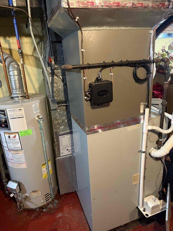 Completed installation of 3-ton air conditioning system with evaporator coil at residential property. Outdoor condenser unit positioned on left side of building with proper electrical connections and conduit installation, while indoor air handler and coil installed in basement mechanical room adjacent to existing water heater. All refrigerant lines connected, electrical wiring completed, system tested and operational upon completion.