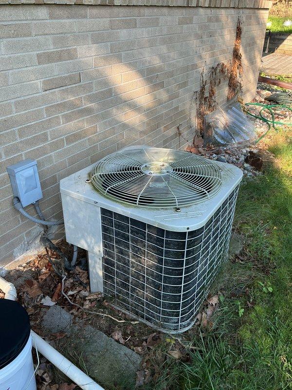 Performed diagnostic evaluation on 28-year-old residential air conditioning system. Unit was reported as still operational and providing cooling despite its age well beyond typical equipment lifespan. Conducted visual inspection of outdoor condensing unit, noting accumulated debris around base and significant rust staining on adjacent brick wall indicating potential historical moisture issues or oxidation from metal components. Verified system operation and confirmed unit continues to function. Documented current condition of aging equipment with photographic records showing wear patterns on protective grille, leaf accumulation at base, and overall unit placement. System remains operational but age indicates replacement should be considered in near-term planning.