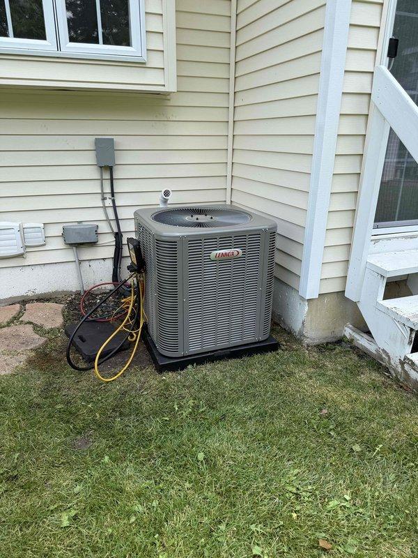 Completed installation of 2.5-ton air conditioning system with evaporator coil at rear of residence. Unit positioned on concrete pad with proper electrical disconnect and conduit installation, PVC condensate drain lines installed with appropriate venting through exterior wall, and all electrical connections completed per code requirements.