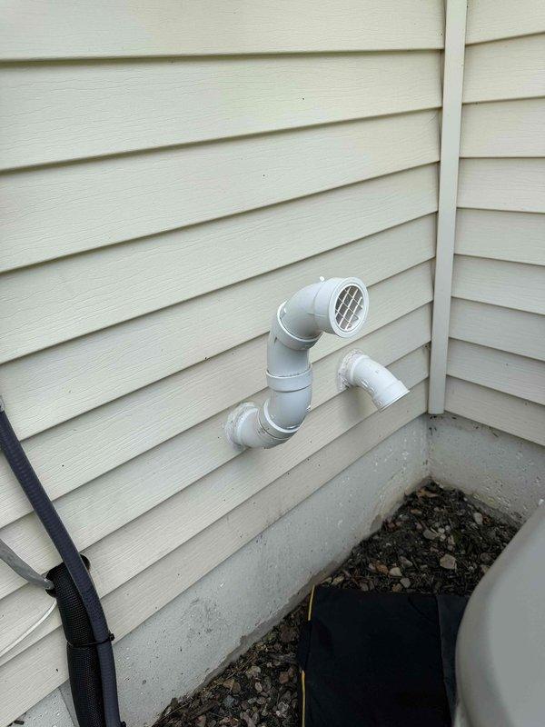 Completed installation of 2.5-ton air conditioning system with evaporator coil at rear of residence. Unit positioned on concrete pad with proper electrical disconnect and conduit installation, PVC condensate drain lines installed with appropriate venting through exterior wall, and all electrical connections completed per code requirements.
