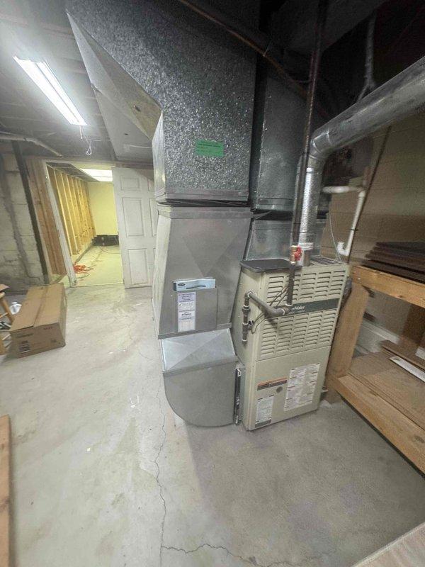 Conducted comprehensive on-site evaluation of existing 16-year-old residential HVAC system including air conditioning unit and furnace located in basement mechanical room. Performed thorough inspection and documentation of current equipment configuration, ductwork layout, and system components to provide accurate full system replacement estimate. Photographed existing furnace with beige cabinet housing, air handler assembly, galvanized supply plenum, and associated ductwork routing for replacement specifications and equipment sizing requirements.