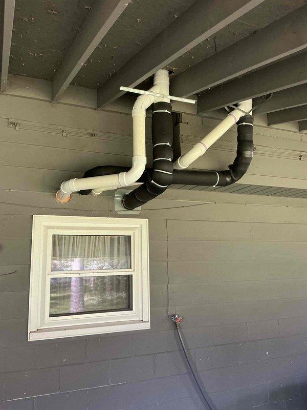 Completed callback service to reconfigure tankless water heater venting system by downsizing from 4" to 3" PVC and installing concentric vent piping through the overhang. Rerouted one of the concentric vents to maintain proper spacing from the adjacent vent line and corrected an intake section that had developed a trap condition. The new 3" concentric vent configuration now properly penetrates the covered porch area with adequate clearance and proper pitch to prevent condensate accumulation.