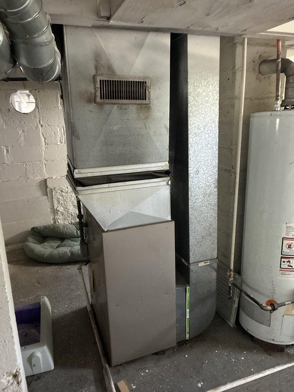 Conducted on-site assessment for whole-house air conditioning system replacement. Evaluated existing HVAC infrastructure in basement mechanical room, including current Payne furnace unit, ductwork configuration, and available space for new equipment installation. Documented existing system layout, electrical service access, and condensate drain routing via PVC piping. Photographed current equipment placement, wall-mounted return air vent, and utility room conditions to develop comprehensive replacement proposal for new AC system installation.