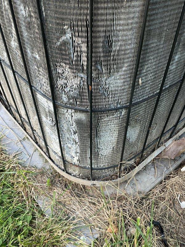 Responded to no cooling complaint with indoor temperature at 78°F despite thermostat set to 69°F. Upon arrival, inspected outdoor condensing unit and found heavily soiled condenser coils with significant dirt, dust, and debris accumulation restricting airflow through the aluminum fins. Wire guard showed overgrown vegetation and organic material around unit perimeter, contributing to reduced system efficiency. Documented condition of outdoor unit with photos showing weathering, mineral deposits, and uneven dirt buildup across coil surfaces. Unit displayed signs of neglected maintenance with unkempt surrounding area affecting performance. Recommended professional coil cleaning and vegetation clearance to restore proper airflow and cooling capacity.