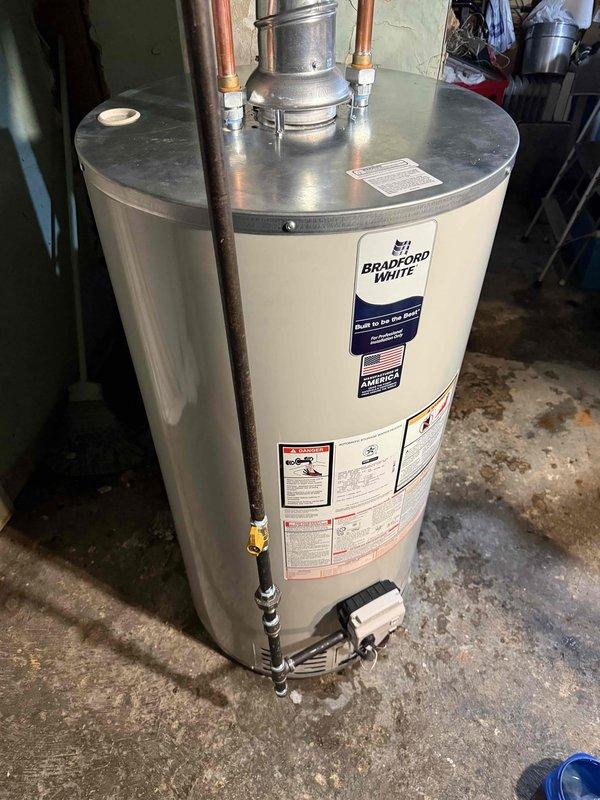 Installed new Bradford White residential tanked water heater in basement utility area on concrete pad. Connected copper supply and return lines with compression fittings, installed gas control valve assembly with black pipe connections, and routed galvanized metal exhaust vent through ceiling opening. All mechanical connections completed per code requirements, pressure relief valve assembly installed with proper discharge piping, and unit tested for proper operation and safety compliance.