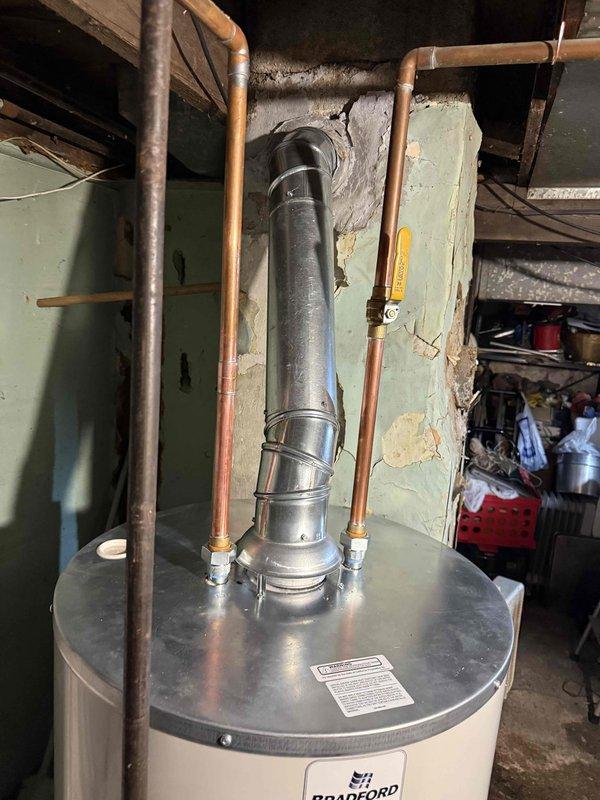 Installed new Bradford White residential tanked water heater in basement utility area on concrete pad. Connected copper supply and return lines with compression fittings, installed gas control valve assembly with black pipe connections, and routed galvanized metal exhaust vent through ceiling opening. All mechanical connections completed per code requirements, pressure relief valve assembly installed with proper discharge piping, and unit tested for proper operation and safety compliance.