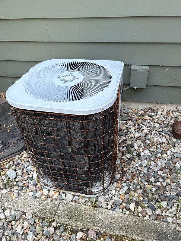 Conducted on-site assessment for complete air conditioning system replacement. Evaluated existing 15-year-old outdoor condenser unit showing significant age-related wear, including weathered metal grille with substantial dirt accumulation and environmental debris. Documented current system configuration with outdoor unit positioned on concrete pad against house foundation, noting electrical disconnect box and conduit connections. Inspected indoor furnace unit and air handler components to determine compatibility requirements for new AC system installation. Photographed existing equipment conditions to support replacement quote preparation for expedited installation scheduling.