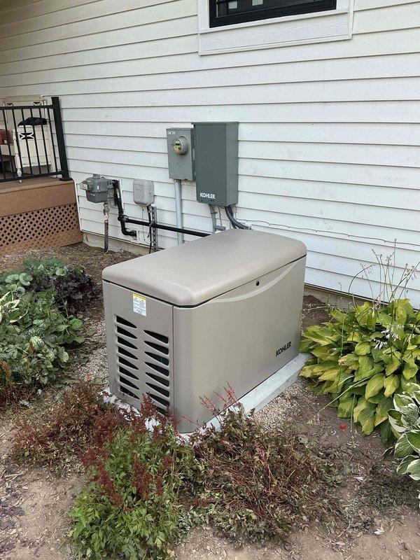 Completed installation of Kohler 20kW residential standby generator (Model 20RCA) with associated transfer switch and electrical connections. Coordinated utility disconnect and reconnect service with power company for safe installation. Generator mounted on prepared gravel base pad adjacent to home exterior, with proper clearances maintained from structure and landscaping. Installed gray Kohler-branded automatic transfer switch on exterior wall with conduit runs connecting to existing electrical meter, generator unit, and home electrical system. All electrical connections completed per manufacturer specifications and local code requirements. Permit obtained and final inspection confirmed successful. Unit tested and operational, ready to provide automatic backup power during utility outages.