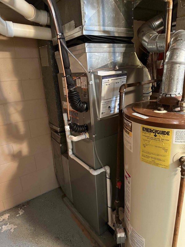 Completed installation of 2-ton air conditioning system with evaporator coil in residential basement mechanical space. New A/C unit positioned at rear location and reconnected to existing furnace system. Installation included proper refrigerant line connections, condensate drainage routing with electronic monitoring device, electrical connections, and integration with existing ductwork. All plumbing connections secured with brass fittings and flexible conduit runs installed per code requirements. System tested for proper operation and airflow distribution throughout residence.