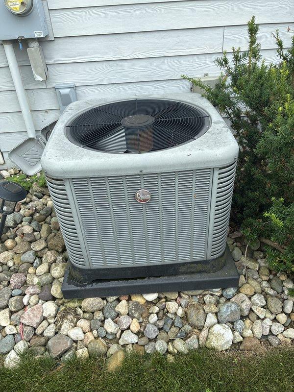 Provided estimate for replacement of 2016 Rheem air conditioning system currently located in basement with outdoor condensing unit positioned on exterior concrete pad with decorative landscaping. Existing unit is operational but customer exploring replacement options. Documented current equipment configuration including electrical connections, refrigerant line routing, and condensate drainage system for proper sizing and installation planning of new system.
