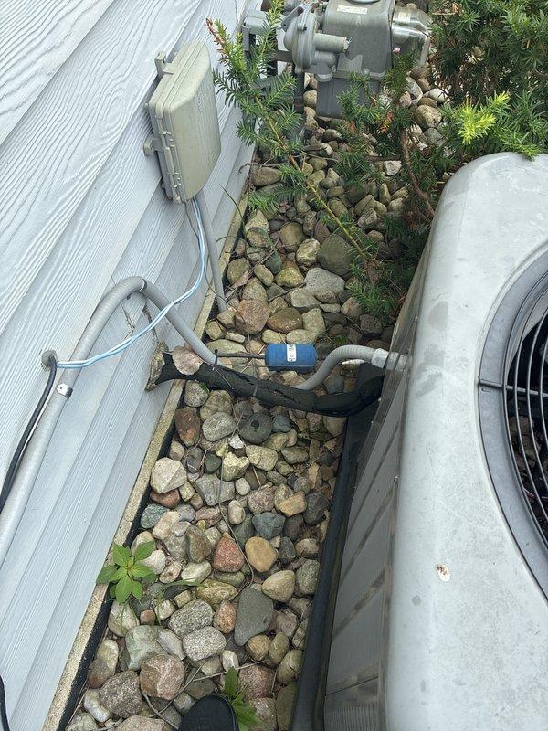 Provided estimate for replacement of 2016 Rheem air conditioning system currently located in basement with outdoor condensing unit positioned on exterior concrete pad with decorative landscaping. Existing unit is operational but customer exploring replacement options. Documented current equipment configuration including electrical connections, refrigerant line routing, and condensate drainage system for proper sizing and installation planning of new system.