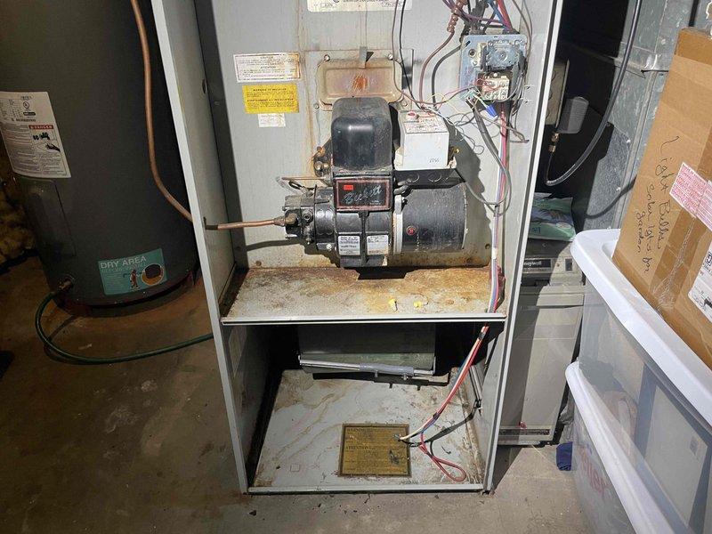 Conducted comprehensive assessment of existing HVAC system for complete replacement estimate. Inspected 40-year-old oil-fired furnace with Beckett burner assembly showing significant age-related wear, accumulated dust, oil staining, and surface discoloration throughout cabinet interior. Evaluated air conditioning system and existing ductwork configuration in basement mechanical room. Documented equipment conditions through detailed photography of furnace cabinet interior, burner components, electrical connections, and surrounding utility area layout. Assessed accessibility for equipment removal and new system installation. Provided recommendations for complete furnace and air conditioning replacement to meet current efficiency standards and customer requirements.