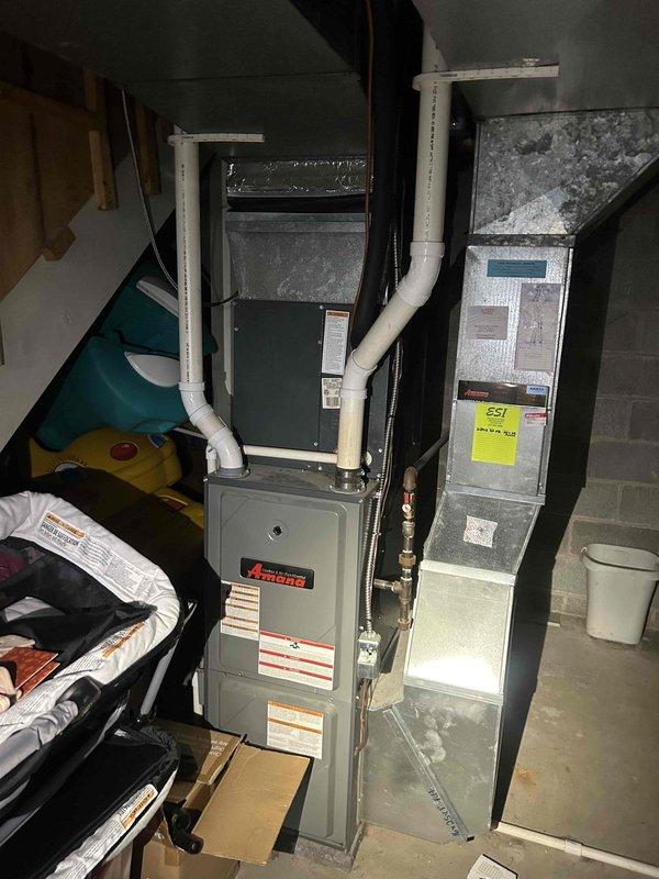 Responded to service call for 10-year-old Amana central air conditioning system experiencing inadequate cooling on main floor during extreme temperatures, while basement maintained proper cooling. Performed comprehensive system evaluation of outdoor condensing unit and indoor air handler/furnace assembly. Inspected outdoor unit positioned on concrete pad, noting weathered cabinet condition consistent with age but operational components. Evaluated refrigerant line routing and electrical disconnect box. Conducted indoor equipment assessment of Amana furnace and air handler unit in basement mechanical room, examining ductwork configuration including white PVC condensate drainage system. Assessed airflow distribution patterns between basement and main floor zones to identify cooling capacity limitations. Provided maintenance recommendations to optimize system performance during peak cooling demands and established preventative maintenance schedule for ongoing system efficiency.