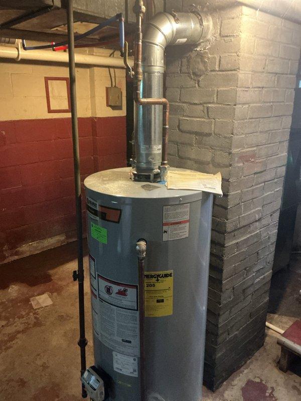 Responded to a no hot water complaint affecting the entire residence from a tank-style water heater that had been experiencing issues for six weeks in a fifty-year-old home. Upon inspection, discovered significant corrosion on the flue assembly mounting flange at the top of the unit, with rust degradation compromising the exhaust ventilation system integrity. Documented the corroded flue components and overall condition of the aging water heater installation, including deteriorated metal surfaces around mounting holes and connection points. The water heater showed signs of extended service life with multiple manufacturer labels visible and standard venting configuration through metal ductwork. Photographed evidence of the compromised exhaust system components and overall unit condition for service records. Recommended replacement of the water heater due to the combination of age-related deterioration, compromised venting components, and ongoing performance issues affecting hot water de