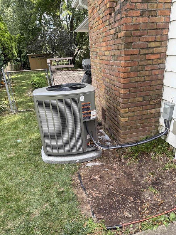 Completed installation of 3.5-ton air conditioning system at residential property. Unit was strategically positioned on concrete pad in front of brick chimney structure in side yard location. New compressor installed and secured to mounting base with refrigerant lines connected and properly routed. All electrical connections completed including disconnect box, system tested and verified operational upon completion.