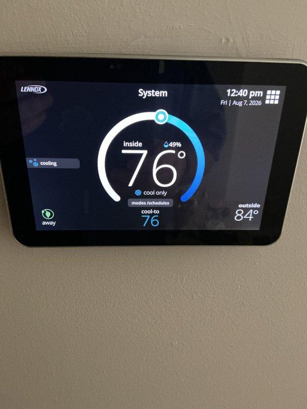 Completed scheduled maintenance on HVAC system including replacement of humidifier pad and air filter. The humidifier pad showed mineral deposits and discoloration from normal use and was replaced with new pad in the black plastic housing frame. Verified proper water distribution through the flexible tubing and confirmed system operation. Thermostat displaying normal cooling operation at 76° setpoint with outdoor temperature at 84°.