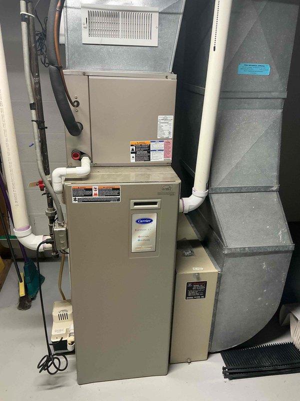 Responded to no-cooling call on Carrier central air conditioning system. Upon arrival, performed diagnostic inspection of HVAC system including furnace and air handler assembly. Documented equipment specifications and current system condition with model number CNPVP2417ALA4AAA, serial number 3112X34592, utilizing Puron refrigerant. System evaluated and photographed for service records showing proper installation configuration with white PVC condensate drainage, ductwork connections, and electrical components in operational condition.
