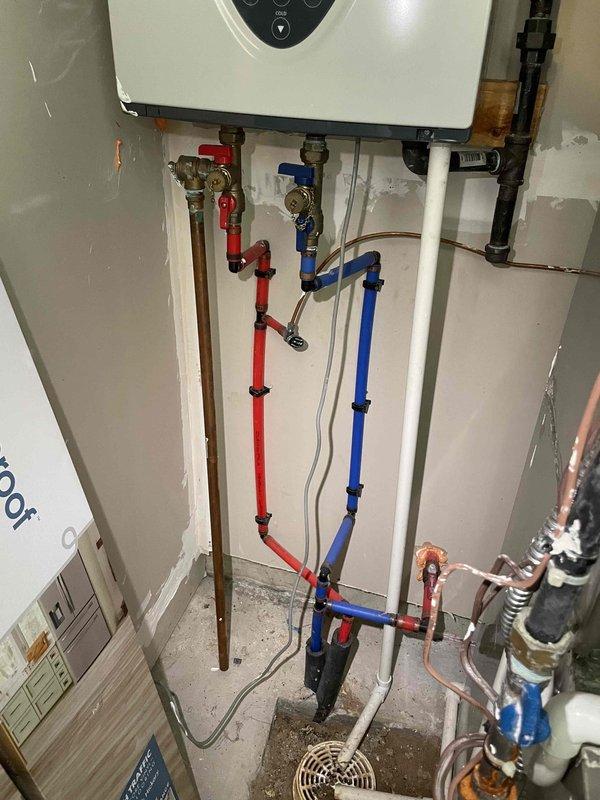 Completed on-site evaluation for replacement of existing gas tank water heater. Assessed current working unit and existing plumbing infrastructure, including wall-mounted equipment with complex PEX and copper supply line configurations, shut-off valves, and pressure relief components. Documented installation specifications for gas-fired water heater replacement, noting natural draft venting requirements and existing mechanical room layout with color-coded hot and cold water distribution systems.