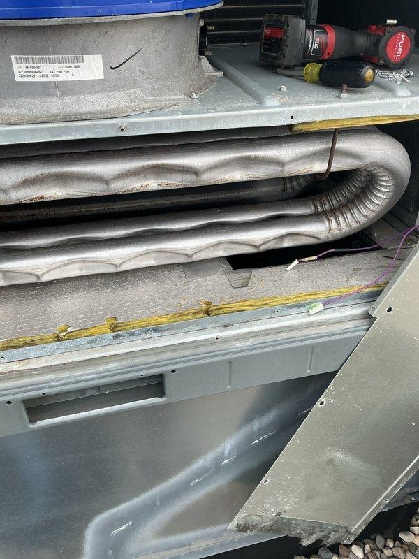 Performed routine maintenance on rooftop HVAC unit, accessing equipment via ladder. Inspected condenser coils and heat exchanger components, noting significant rust and corrosion on upper curved refrigerant pipes and metallic fins throughout the unit. Examined internal components including refrigerant line coils, metal panels, and seals, observing age-related deterioration and moisture exposure. Documented equipment condition through photographic evidence showing extensive rust damage on coil surfaces and general wear patterns consistent with environmental exposure.