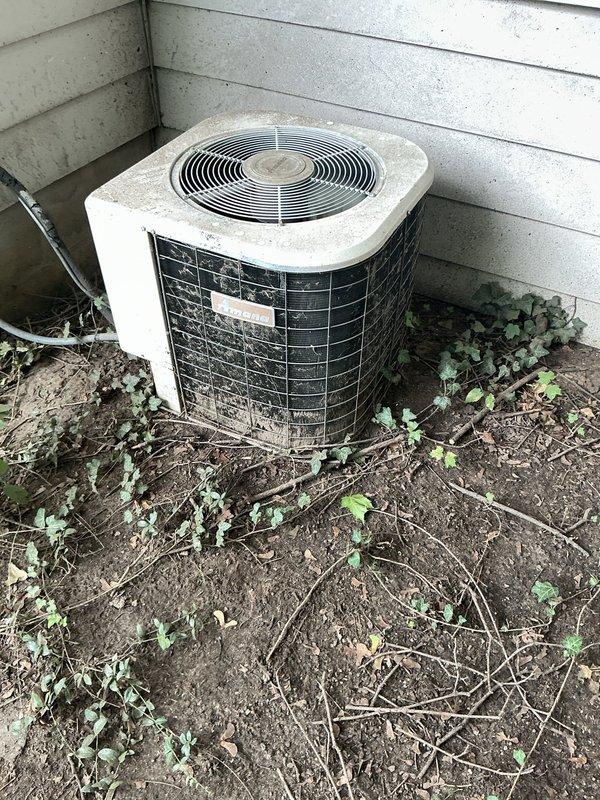 Responded to service call for outdoor AC condenser unit running loudly but still cooling effectively. Upon inspection, found significant debris accumulation around unit base including leaves, twigs, and vegetation growth impeding proper airflow. Observed exposed electrical wiring emerging from damaged section of base housing, creating potential safety hazard. Cleared organic debris from around condenser unit perimeter and verified fan operation and airflow through coil sections. Condenser coils showed weathering and dirt buildup on exterior surfaces. Advised customer that exposed wiring requires proper sealing and that debris accumulation likely contributing to excessive noise levels, though compressor and fan assembly continuing to function and maintain adequate cooling capacity.