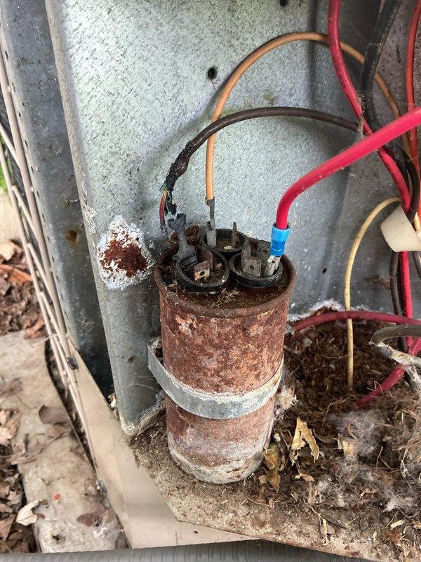 # HVAC Service Completed

Responded to service call for 16-year-old central air conditioning system with reduced cooling capacity. Customer reported unit operating but not achieving previous temperature levels. Upon arrival, performed comprehensive system diagnostic and visual inspection of outdoor condensing unit.

Inspection revealed severely corroded outdoor electrical capacitor with extensive rust and oxidation throughout the metal housing. The capacitor showed significant deterioration from prolonged weather exposure, with corrosion affecting the cylindrical body and mounting components. Connected wiring displayed age-related wear with visible insulation degradation. Heavy accumulation of organic debris, leaves, and dirt observed around capacitor base and equipment foundation.

Examined main electrical enclosure box, noting substantial dirt and grime buildup on transparent viewing window with green, brown, and yellow staining obscuring interior visibility. Exterior casing showed w