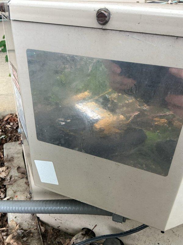 # HVAC Service Completed

Responded to service call for 16-year-old central air conditioning system with reduced cooling capacity. Customer reported unit operating but not achieving previous temperature levels. Upon arrival, performed comprehensive system diagnostic and visual inspection of outdoor condensing unit.

Inspection revealed severely corroded outdoor electrical capacitor with extensive rust and oxidation throughout the metal housing. The capacitor showed significant deterioration from prolonged weather exposure, with corrosion affecting the cylindrical body and mounting components. Connected wiring displayed age-related wear with visible insulation degradation. Heavy accumulation of organic debris, leaves, and dirt observed around capacitor base and equipment foundation.

Examined main electrical enclosure box, noting substantial dirt and grime buildup on transparent viewing window with green, brown, and yellow staining obscuring interior visibility. Exterior casing showed w