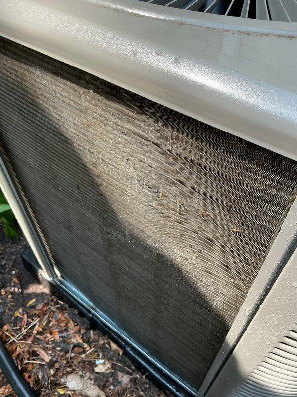 Completed annual heating and cooling maintenance on residential air conditioning condenser unit. Performed comprehensive system inspection including visual assessment of outdoor unit cabinet, fan assembly, and condenser coils. Documented heavy soiling and debris accumulation on heat exchanger fins with significant discoloration present, particularly on intake side of coil. Verified refrigerant line connections and insulation integrity on suction and liquid lines. Inspected condensate drain line routing and unit mounting on concrete pad. Unit operational at time of inspection with fan assembly functioning properly.