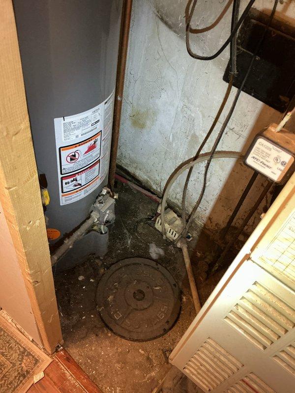 Responded to service call for leaking hot water tank in basement utility area. Upon arrival, found significant water accumulation on concrete floor surrounding base of gray cylindrical water heater. Performed diagnostic inspection of unit and all associated connections, including copper supply lines, brass fittings, and discharge piping. Identified active leak condition requiring attention. Documented existing conditions including wet floor, plumbing configuration, and water heater installation setup. Completed diagnostic evaluation of tanked water heater system and provided findings to customer regarding leak source and recommended corrective actions.
