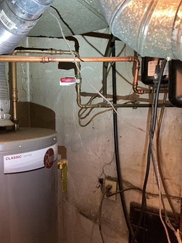 Responded to service call for leaking hot water tank in basement utility area. Upon arrival, found significant water accumulation on concrete floor surrounding base of gray cylindrical water heater. Performed diagnostic inspection of unit and all associated connections, including copper supply lines, brass fittings, and discharge piping. Identified active leak condition requiring attention. Documented existing conditions including wet floor, plumbing configuration, and water heater installation setup. Completed diagnostic evaluation of tanked water heater system and provided findings to customer regarding leak source and recommended corrective actions.