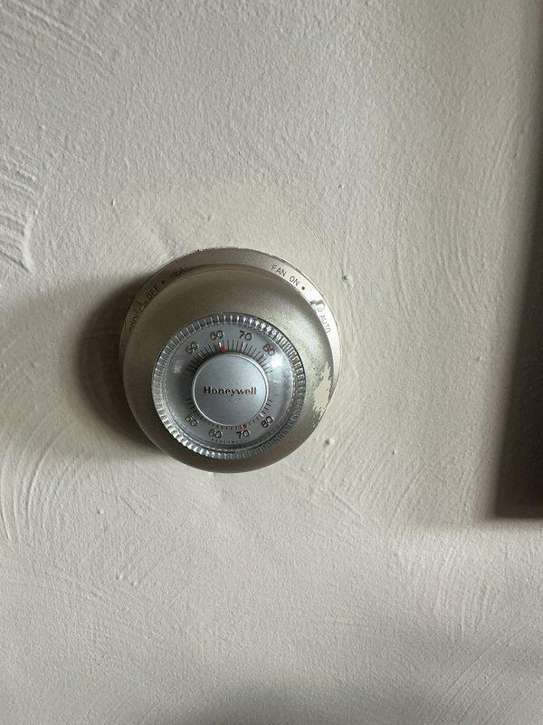 Completed comprehensive HVAC tune-up inspection on 5-year-old air conditioning system located outdoors. Performed thorough evaluation of thermostat operation, verifying proper functionality of Honeywell mechanical round-style unit with manual temperature adjustment capabilities. Inspected and documented air filtration system, noting accumulated dust and debris on pleated filter material requiring attention. Conducted standard maintenance checks including humidifier inspection and hot water tank evaluation as part of routine seasonal maintenance protocol. All components assessed for proper operation and system performance verified.