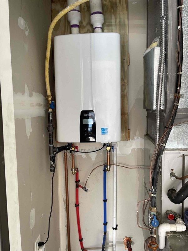 Completed installation of Navien NPE-240A2 tankless water heater in mechanical room. Mounted unit to wall, connected hot and cold water supply lines using PEX piping with appropriate shut-off valves and brass fittings, installed yellow flexible gas line connection, and ran white PVC exhaust and intake venting through exterior wall. Established electrical connection and configured digital control panel. Modified floor drain area with PVC drainage piping to accommodate condensate discharge requirements. All connections tested and verified for proper operation. Installation completed in accordance with manufacturer specifications and local mechanical permit requirements.