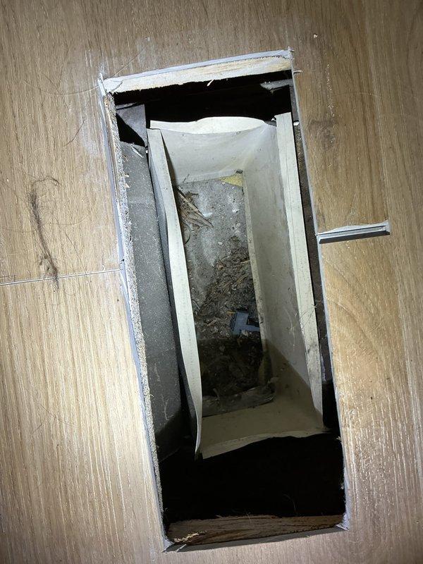 Responded to service call for poor airflow on a 15-year-old air conditioning system that was still cooling but experiencing reduced air delivery. Upon inspection, accessed the underfloor ductwork through existing floor opening to examine the supply duct system. Found metal ductwork beneath flooring with visible dust and debris accumulation on interior surfaces, which was contributing to restricted airflow. Documented conditions of both the floor access point and the metal duct assembly showing signs of age-related deterioration and contamination. System evaluation confirmed cooling capacity remained functional despite compromised air distribution through the duct system.
