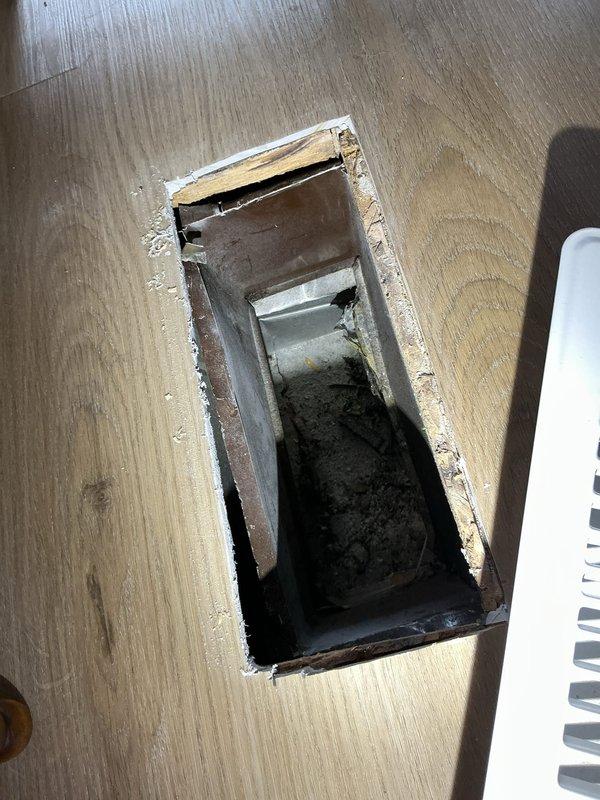 Responded to service call for poor airflow on a 15-year-old air conditioning system that was still cooling but experiencing reduced air delivery. Upon inspection, accessed the underfloor ductwork through existing floor opening to examine the supply duct system. Found metal ductwork beneath flooring with visible dust and debris accumulation on interior surfaces, which was contributing to restricted airflow. Documented conditions of both the floor access point and the metal duct assembly showing signs of age-related deterioration and contamination. System evaluation confirmed cooling capacity remained functional despite compromised air distribution through the duct system.