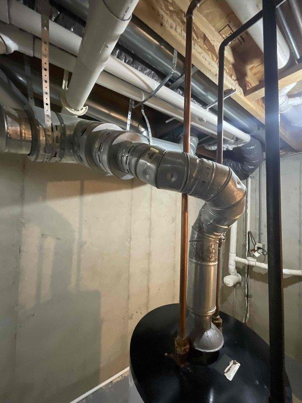 Conducted on-site assessment for standard water heater replacement in basement utility area. Existing natural draft water heater experiencing leak from bottom of tank, requiring full unit replacement. Evaluated existing plumbing configuration, venting system with metal flue pipe, and surrounding infrastructure including water meter, copper supply lines, and PVC drainage to provide comprehensive replacement estimate.