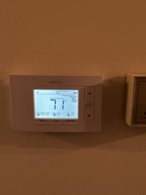 Completed comprehensive ComfortGuard Maintenance Package including full system inspection and preventative maintenance procedures. Verified thermostat operation with Sensi digital unit displaying proper temperature readings at 71°F ambient with setpoint of 75°F and humidity level at 55%, confirmed all control functions and programming settings operational. Inspected and documented air filtration system with diamond mesh filter showing moderate dust accumulation, recommended filter replacement at next service interval due to debris buildup along top edge and visible oxidation on metal frame housing.