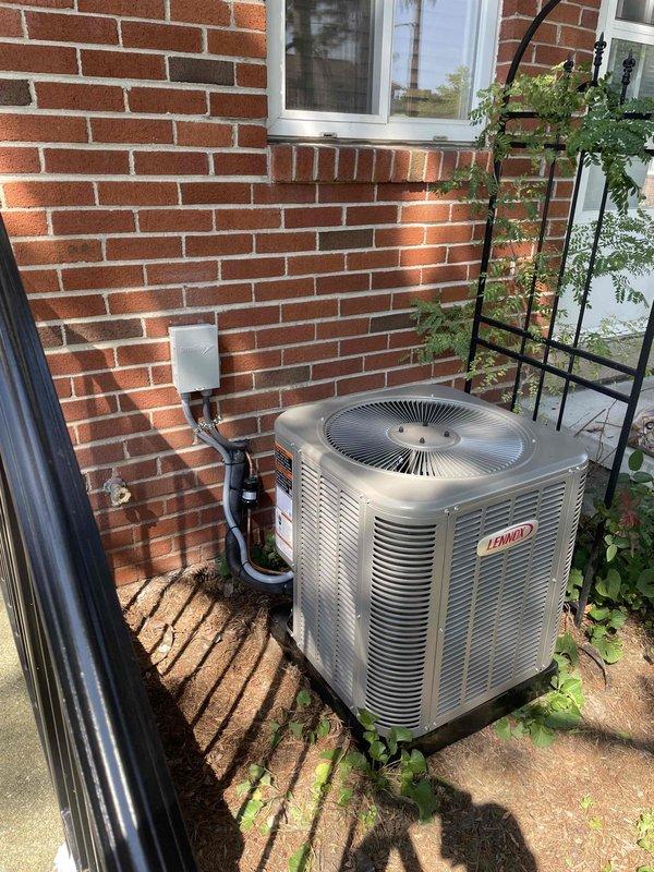 Completed full installation of Lennox air conditioning system and evaporator coil at residential property. Outdoor condensing unit positioned on concrete pad against exterior brick wall with proper electrical disconnect and conduit installation. Indoor evaporator coil installed in ductwork system between ceiling joists with metallic supply plenum connections, secured with metal bands and proper sealing at all joints. All ductwork connections completed with rigid and flexible components as required. System installed per manufacturer specifications and ready for operation.